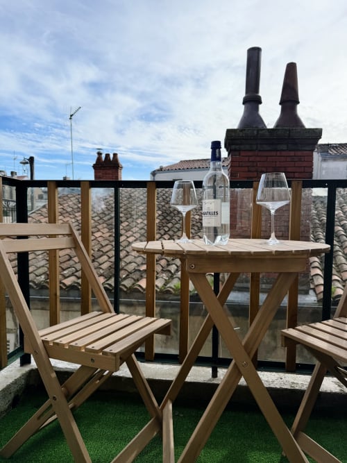 Terrasse sur le toit de l'appartement ARLOÉ à La Rochelle avec bouteille de vin, verres, mobilier en bois et vue sur la ville
