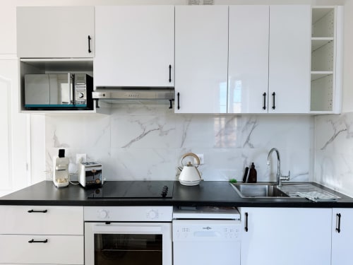 Cuisine moderne blanche avec plan de travail noir, crédence en marbre et électroménagers en acier inoxydable à l'appartement ARLOÉ