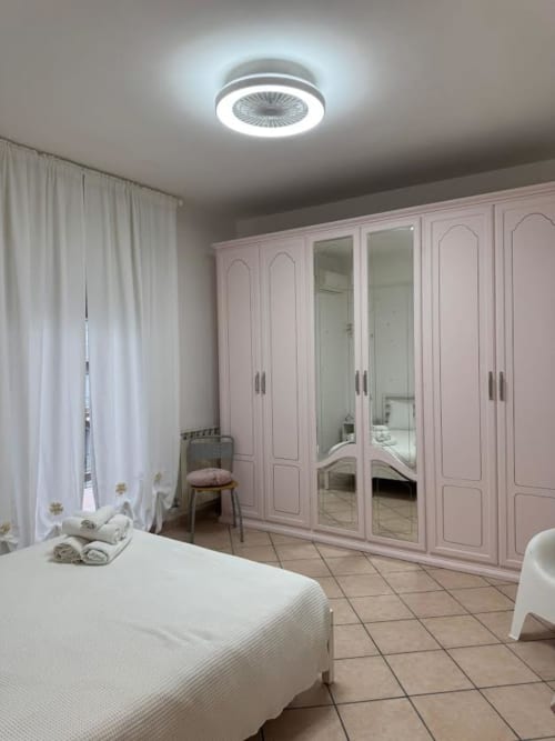 Quarto moderno em apartamento de Catânia com guarda-roupa rosa, cama branca e ventilador de teto com iluminação