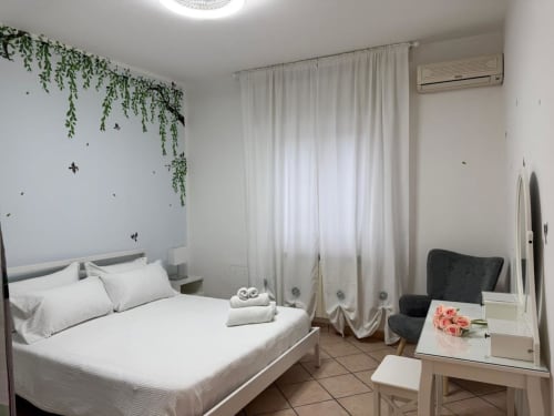 Quarto iluminado no B&B I Mori em Catania com cama branca, plantas suspensas, cortinas e móveis modernos