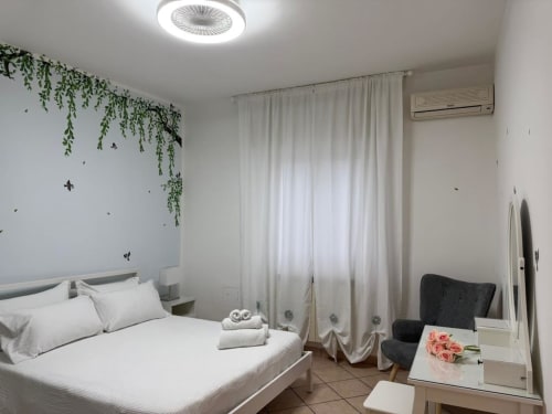Quarto moderno e luminoso na Pousada Catania com cama branca, plantas suspensas verdes, cortinas, ar-condicionado e espelho