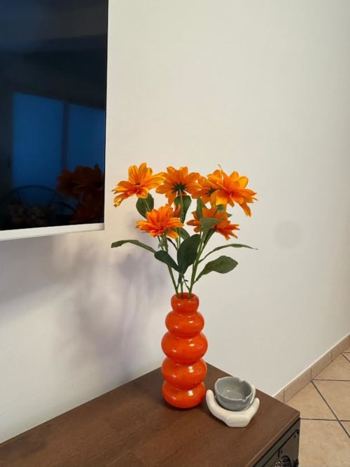 Gérberas laranja brilhantes em vaso vermelho sobre mesa no apartamento B&B Catania