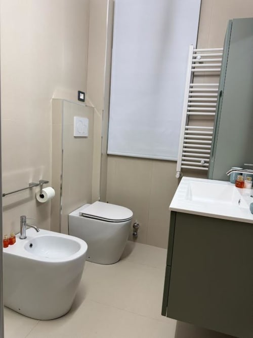 Banheiro moderno em apartamento em Catania com bidê branco, vaso sanitário, pia e gabinete verde