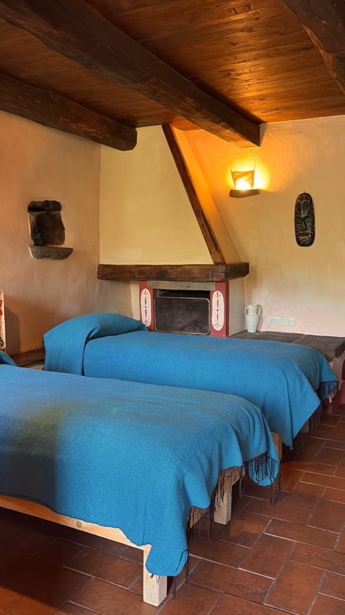 Rustieke slaapkamer in Podere di Maggio met houten balkenplafond, twee blauwe bedden, open haard en traditionele inrichting in Santa