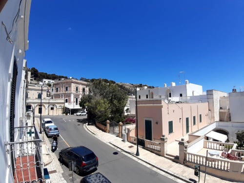 Via di Santa Cesarea Terme con edifici mediterranei, appartamenti rosa e bianchi, cielo azzurro e pendio collinare