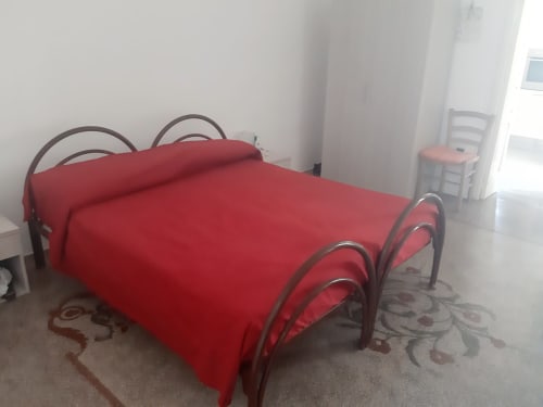 Camera da letto luminosa con biancheria rossa e letto in metallo presso l'appartamento Santa Cesarea Vacanze, Italia