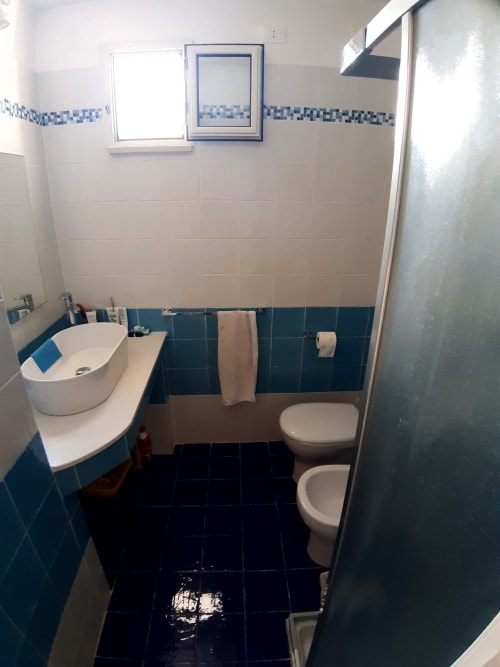 Bagno dell'appartamento Santa Cesarea Vacanze con piastrelle blu e bianche, lavabo bianco, water e box doccia