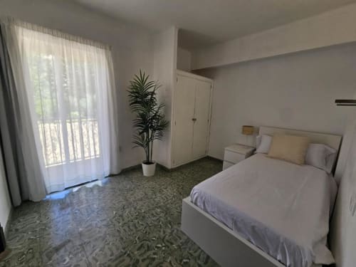 Habitación individual de lujo en Villa Palmer Paguera con cama, armario blanco, planta en maceta y puertas al balcón con cortinas translúcidas