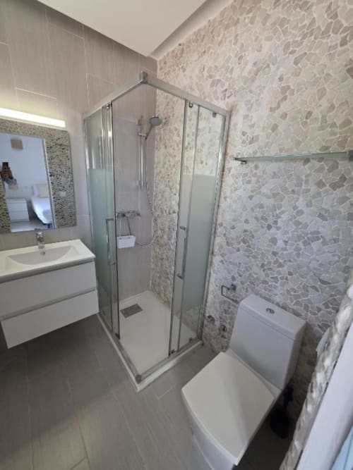 Baño moderno en Villa Palmer Paguera con ducha de cristal, lavamanos blanco, inodoro y azulejos decorativos de mosaico