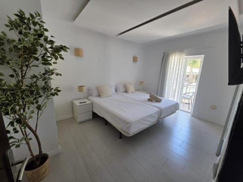 Moderna habitación doble en la Villa Palmer de Paguera con dos camas, ropa blanca, planta en maceta, acceso a balcón y suelo de baldosas