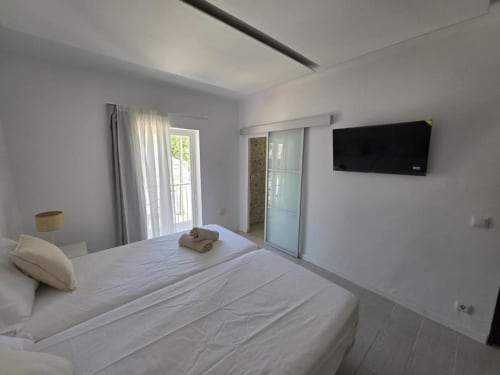 Moderna habitación doble en Villa Palmer hostel de Paguera con ropa de cama blanca, TV pantalla plana, acceso a balcón y diseño minimalista