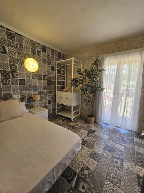 Elegante habitación individual en Villa Palmer hostel, Paguera, con azulejos decorativos, cama blanca, estanterías de madera y balcón