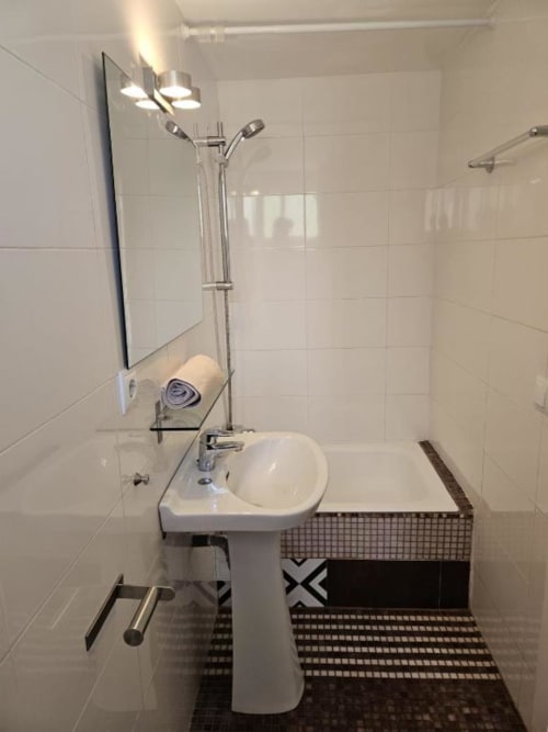Baño moderno en el hostal Villa Palmer Paguera con lavamanos pedestal, ducha, azulejos blancos y patrón blanco y negro