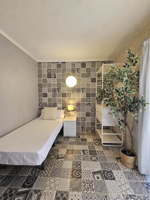 Habitación individual compacta en el hostal Villa Palmer de Paguera con cama, azulejos decorativos, planta en maceta y mobiliario moderno