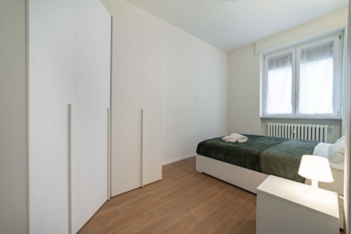 Camera da letto moderna dell'appartamento La Magnolia a Firenze - letto con biancheria verde, guardaroba bianco, pavimento in legno, finestra con vista sul giardino