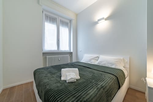 Camera da letto moderna nell'appartamento La Magnolia di Firenze, con letto matrimoniale con biancheria a righe verdi, ampia finestra e radiatore