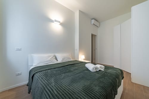 Camera da letto moderna nell'appartamento La Magnolia a Firenze, con letto trapuntato verde, cuscini bianchi e arredamento minimalista