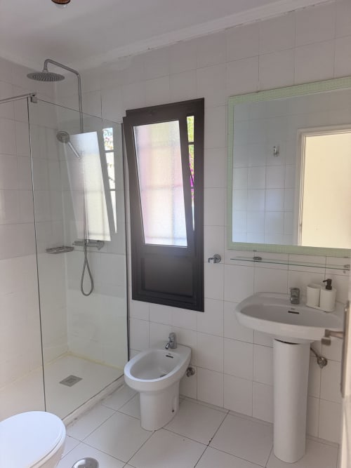 Baño moderno con mamparas de ducha de cristal, inodoro, bidé y lavabo pedestal en apartamento Kamalahouse SL de Corralejo