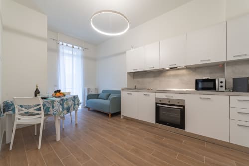 Moderno appartamento a Firenze con cucina e zona living: mobili bianchi, pavimenti in legno, poltrona blu e tavolo da pranzo