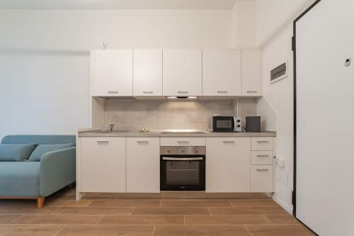 Cucina moderna bianca con forno incassato nell'appartamento La Magnolia a Firenze. Divano blu visibile a sinistra, pavimento in legno