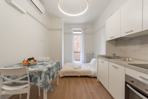 Moderno monolocale a Firenze con angolo cottura, tavolo da pranzo, letto e vista giardino attraverso porta in vetro