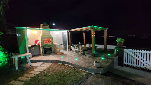 Área de entretenimento externa da villa Philia à noite, Florianópolis, com lareira, assentos, pérgula verde e vista para o mar