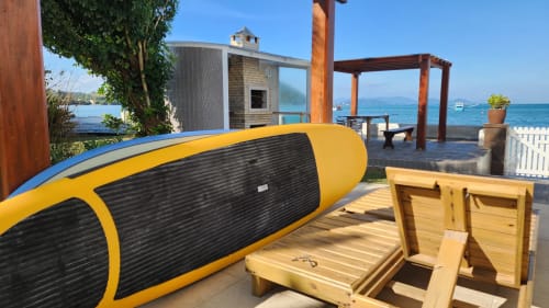 Prancha de surfe amarela e preta no deck de madeira do hotel Philia em Florianópolis com vista para o mar e arquitetura moderna de villa