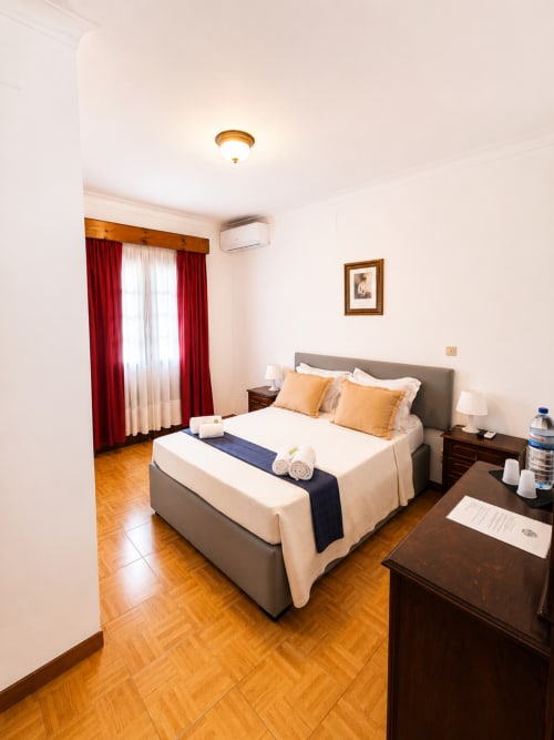 Quarto duplo da Serrana Gerês Inn com vista para a montanha, cama cinza, móveis em madeira, cortinas vermelhas e ar condicionado