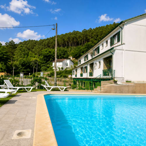 Piscina da Pousada Serrana Gerês com vista para as montanhas, espreguiçadeiras brancas e edifício branco com venezianas verdes em Gerês