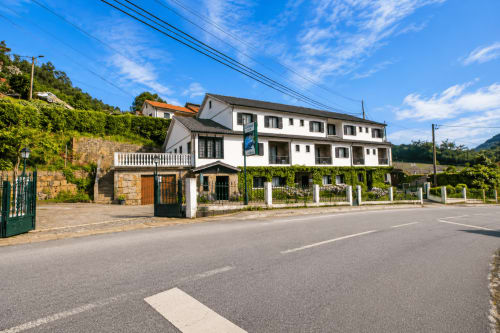 Exterior da Serrana Gerês Inn em aldeia montanhosa, edifício branco com persianas verdes e vistas para as montanhas em Gerês
