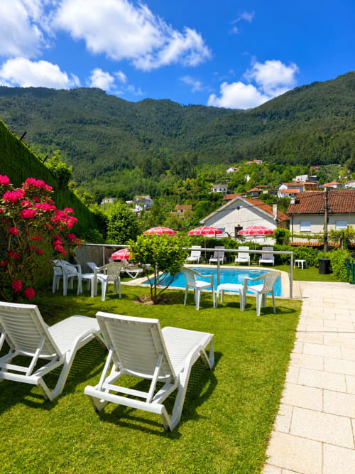Área de piscina da Serrana Gerês Inn com espreguiçadeiras, guarda-sóis rosa e vistas da serra em Gerês, Portugal