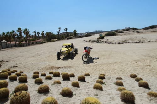 Buggy amarillo y moto roja estacionados en arena del desierto con cactus en Vidasoul BnB en La Vinorama, México