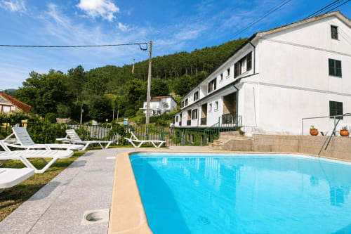Piscina da Pousada Serrana Gerês com espreguiçadeiras brancas, edifício branco e montanhas florestadas em Gerês, Portugal