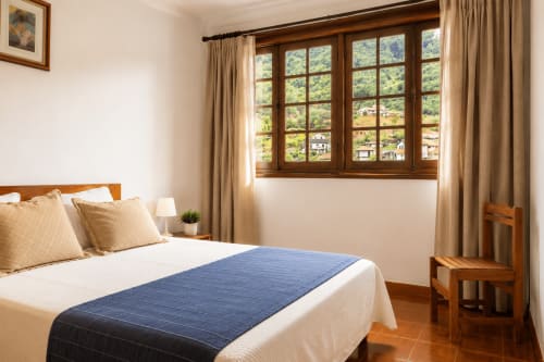 Quarto luminoso na Pousada Serrana Gerês com cama de madeira, roupa de cama azul, vista para as montanhas pelas grandes janelas e decoração tradicional