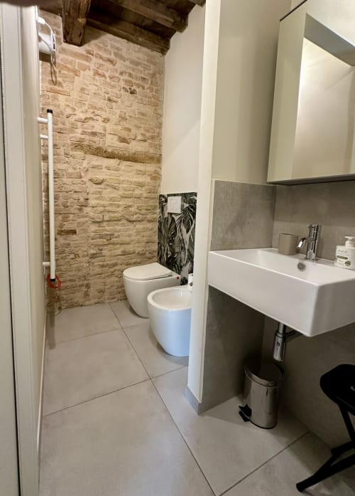 Modern bathroom at NOUA LIVING Suite 3, Ravenna: white sink, toilet, brick walls, tiled floor