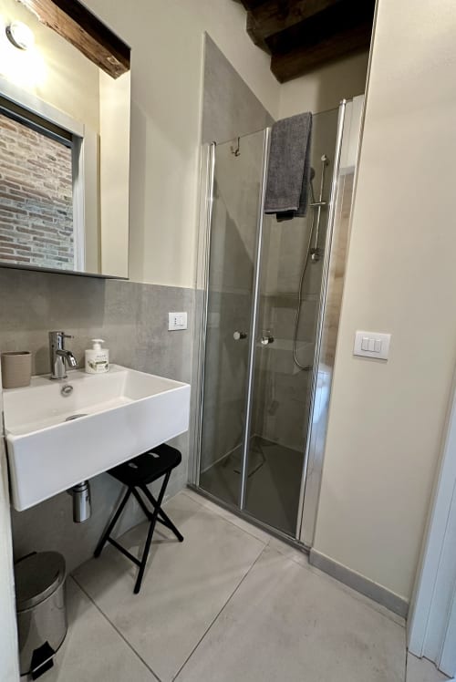 Modern bathroom in NOUA LIVING apartment suite in Ravenna with white sink, glass shower enclosure, and gray tile accents