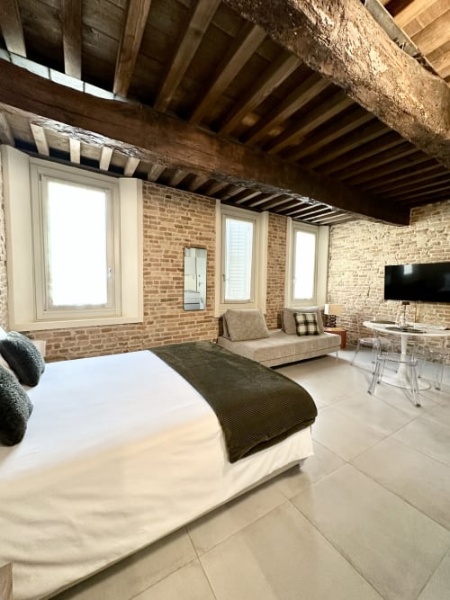 Suite in stile loft moderno presso NOUA LIVING Ravenna con mattoni a vista, travi in legno, letto, divano e finestre dal pavimento al soffitto