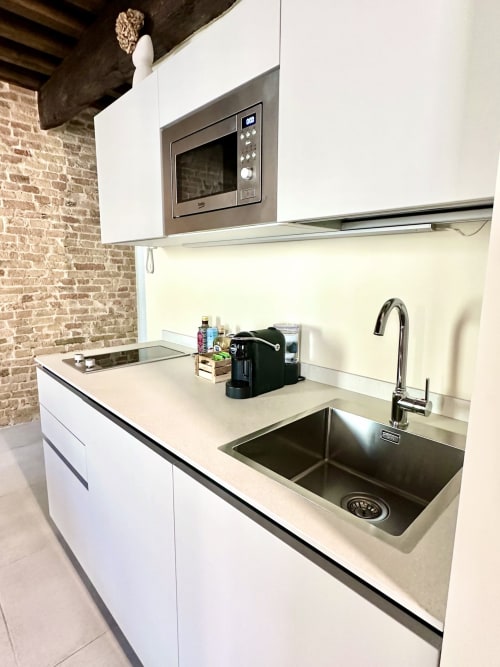 Cucina moderna bianca con lavello in acciaio inossidabile, microonde e piano di lavoro color crema nell'appartamento NOUA LIVING di Ravenna