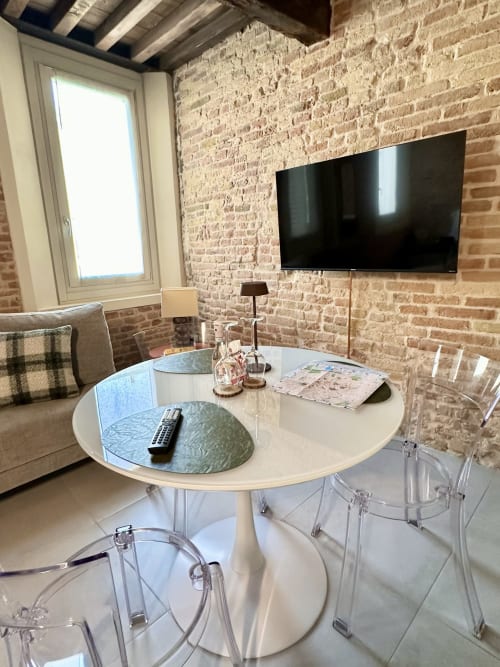 Soggiorno moderno nella Suite 4 NOUA LIVING Ravenna con tavolo rotondo, sedie trasparenti, muri in laterizio a vista e arredamento murale