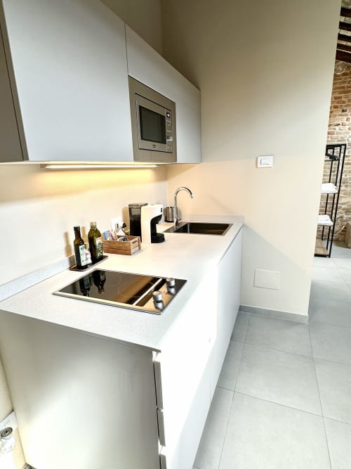 Cucina bianca moderna nell'appartamento NOUA LIVING di Ravenna con piano cottura, lavello, microonde e bancone da pranzo