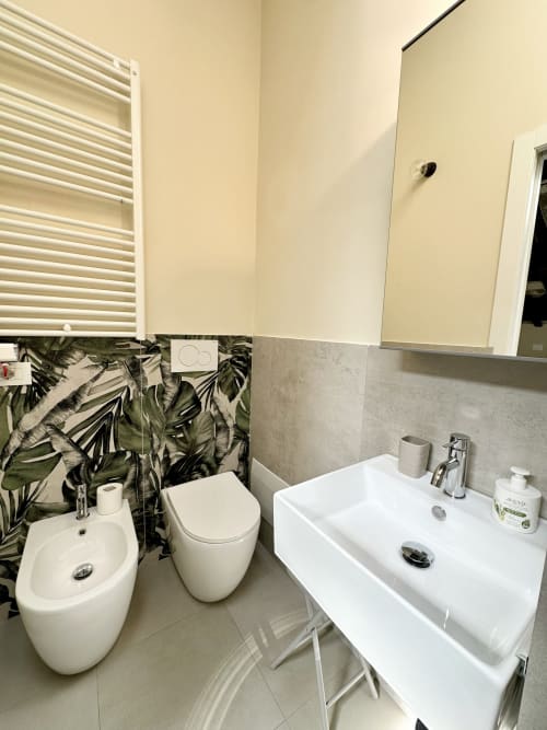 Moderno bagno NOUA LIVING Ravenna con bidet e lavabo bianchi, dettagli di piastrelle tropicali, scaldasalviette riscaldato