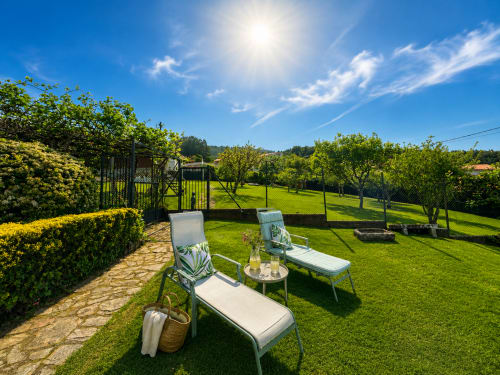 Jardín soleado de la casa Mar y Sol en Baiona con tumbonas, mesa, césped verde, árboles y vistas al mar