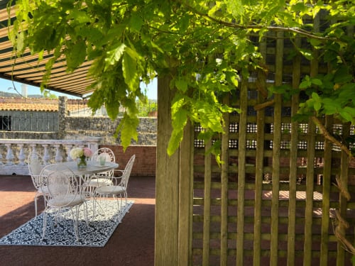 Terraza sombreada con muebles blancos y pérgola de enredadera verde con vistas a los jardines de la casa rural de Baiona