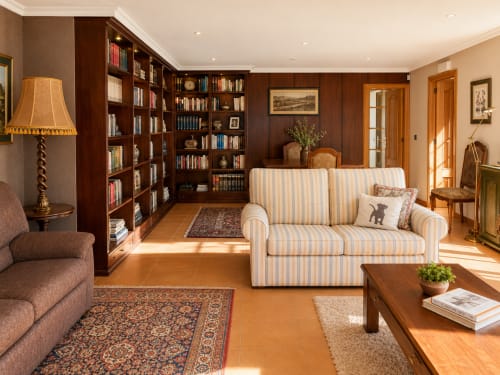 Elegante salón biblioteca en  Baiona con sofá a rayas, librerías de madera oscura y vistas al mar