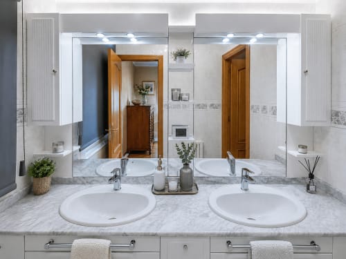 Lujoso baño con doble lavamanos en la casa Holibai de Baiona con encimeras de mármol, espejos iluminados y vistas al mar