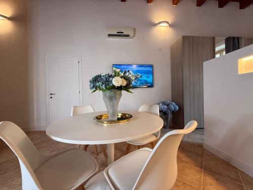 Zona pranzo moderna nell'appartamento Casa Cavour di Casa Lounge Istria, Cagliari con tavolo rotondo, sedie bianche, fiori e TV