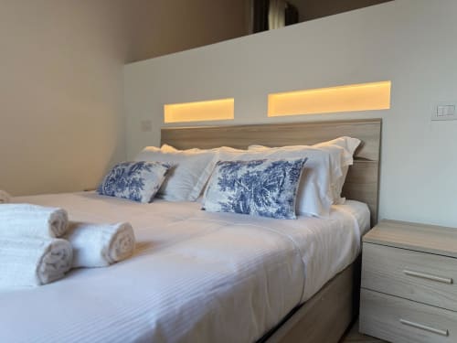Camera moderna di Casa Lounge Istria a Cagliari con letto matrimoniale, cuscini blu decorati e illuminazione calda