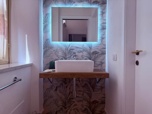 Bagno moderno di Casa Lounge Istria a Cagliari con specchio illuminato, lavabo bianco su vanity in legno e dettagli botanici