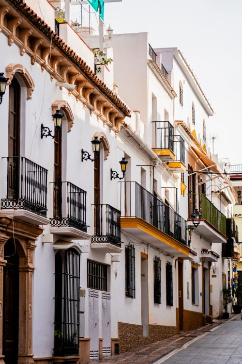 Historic whitewashed street in Elviria with ornate wooden details and black balconies near HomyMarbella hotel