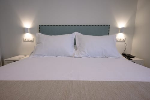 Moderno dormitorio del hotel Alcazaba Salobreña con ropa de cama blanca, cabecero turquesa y lámparas de mesita en Granada, España